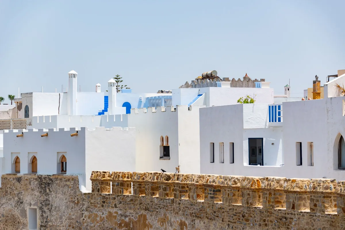 Des maisons blanches aux détails bleus qui s'élèvent derrière les remparts de pierre d'Asilah