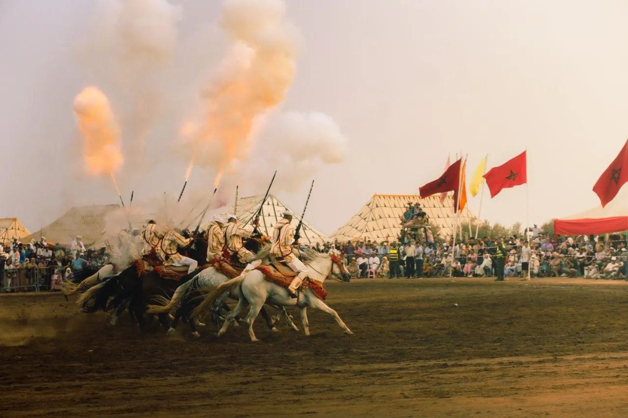 Fantasia riders at full gallop, firing their rifles into the sky in front of the crowd