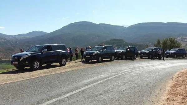 Black 4×4s stopped by a mountain road, with their passengers beside them