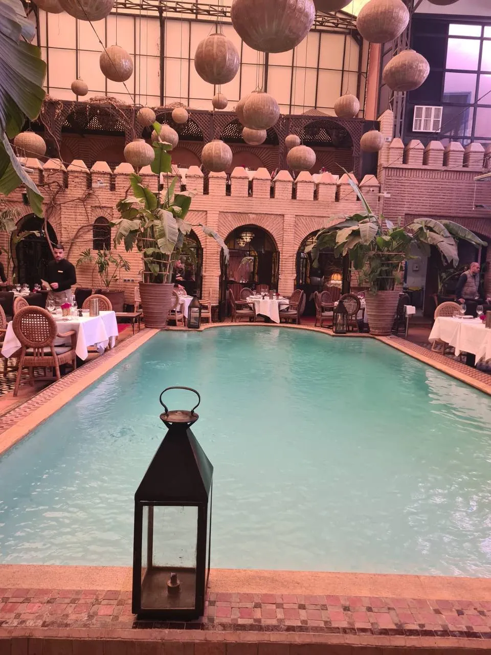 The tables of a palace restaurant set around a pool, under hanging lanterns