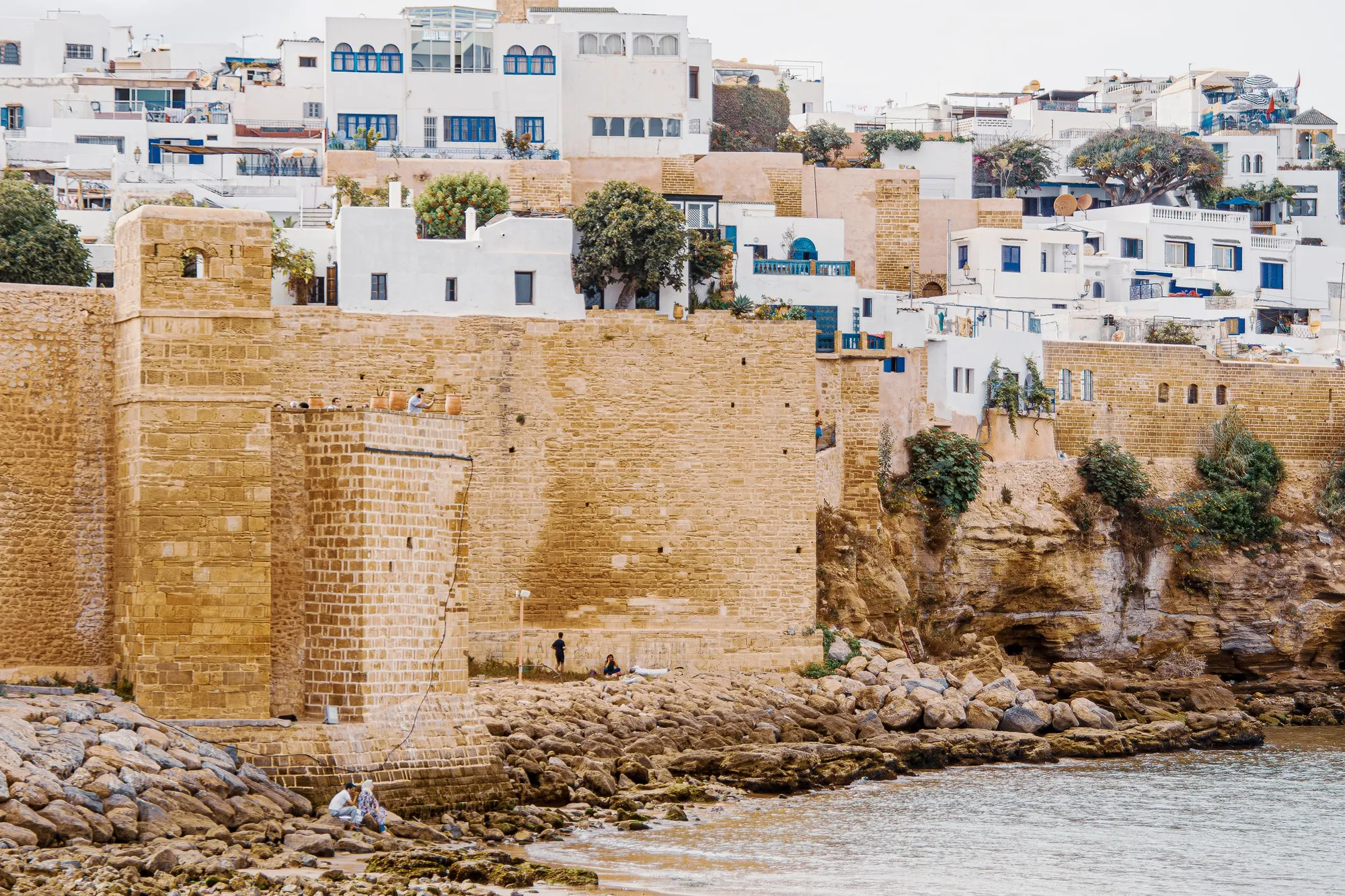 Les remparts de pierre de la kasbah des Oudayas dominant les rochers et l'eau, avec des maisons blanches et bleues derrière