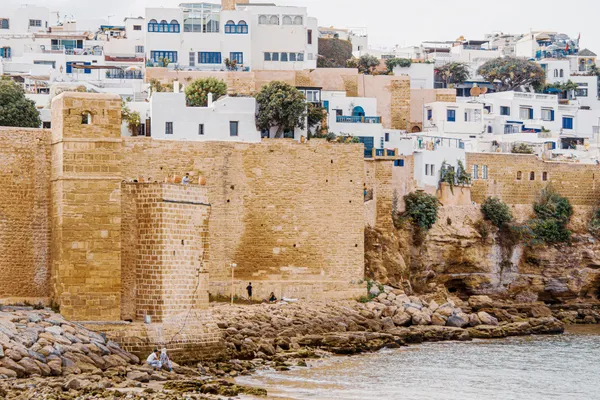 Les remparts de pierre de la kasbah des Oudayas dominant les rochers et l'eau, avec des maisons blanches et bleues derrière