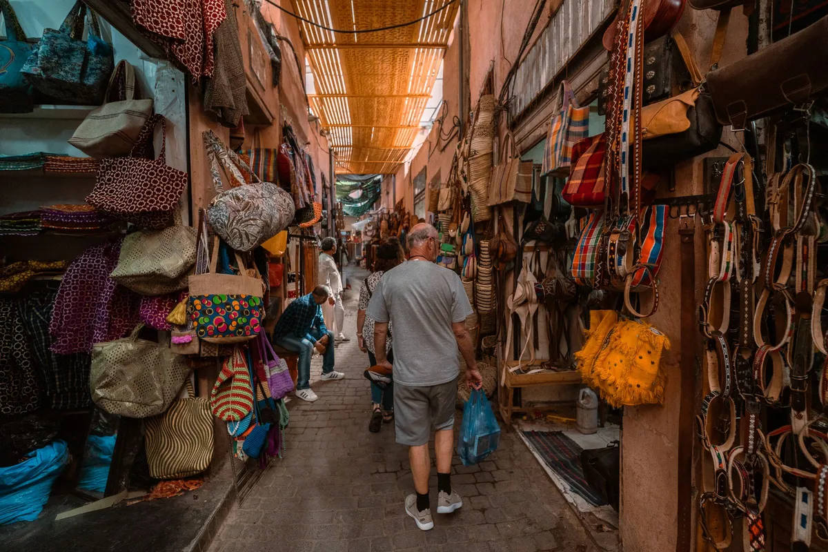 A narrow covered lane of the souk lined with hanging bags and leather goods, with a visitor walking between the stalls